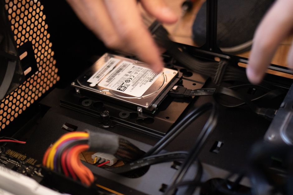 A close-up of a person installing a Solid-State Drive (SSD) into an open laptop, symbolizing a budget tech upgrade.