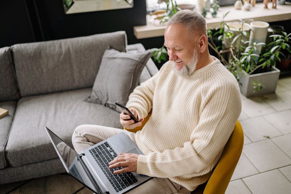 A person sitting at a cafe table, focused on a laptop with a smartphone nearby, indicating remote work or leisure use in a public setting.