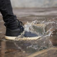 A person wearing dark, comfortable footwear winter boots navigating a wet, leaf-strewn city pavement, emphasizing practicality and grip for urban environments.