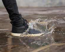 A person wearing dark, comfortable footwear winter boots navigating a wet, leaf-strewn city pavement, emphasizing practicality and grip for urban environments.