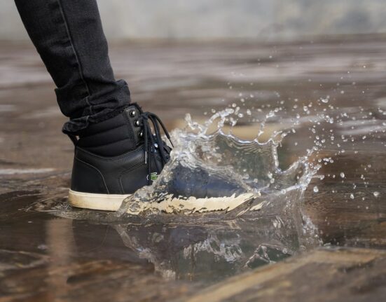 A person wearing dark, comfortable footwear winter boots navigating a wet, leaf-strewn city pavement, emphasizing practicality and grip for urban environments.