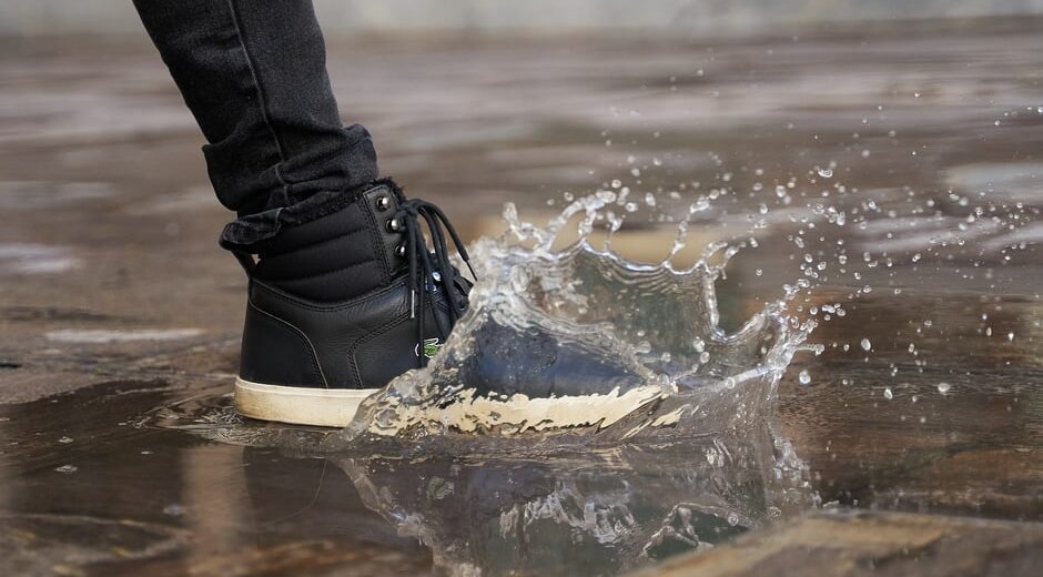 A person wearing dark, comfortable footwear winter boots navigating a wet, leaf-strewn city pavement, emphasizing practicality and grip for urban environments.