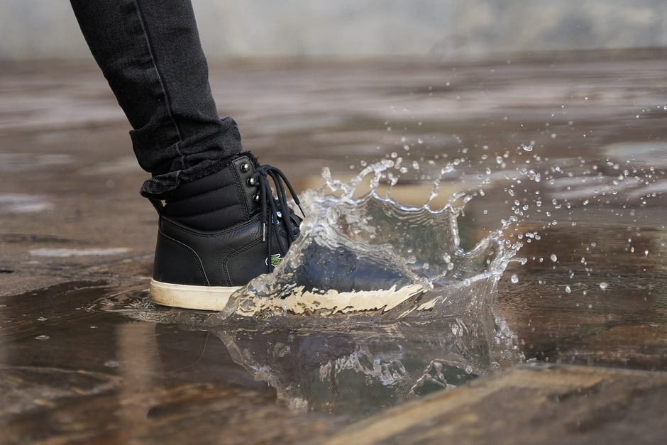 A person wearing dark, comfortable footwear winter boots navigating a wet, leaf-strewn city pavement, emphasizing practicality and grip for urban environments.