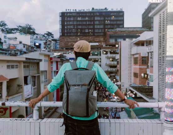 A person wearing a grey anti-theft backpack walking through a busy city street with historical buildings in the background, demonstrating active urban use.