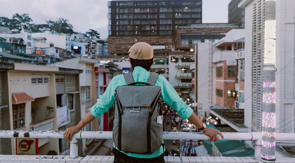 A person wearing a grey anti-theft backpack walking through a busy city street with historical buildings in the background, demonstrating active urban use.