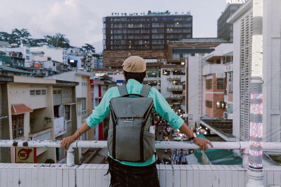 A person wearing a grey anti-theft backpack walking through a busy city street with historical buildings in the background, demonstrating active urban use.