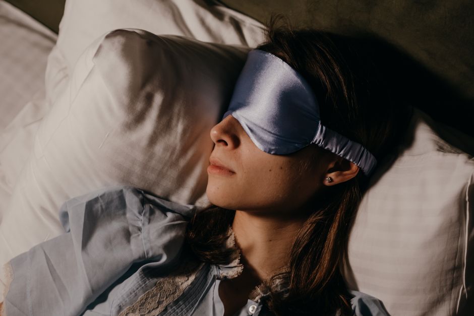 A person comfortably resting on a long-haul flight, wearing a soft eye mask and a supportive neck pillow, hinting at the importance of rest for beauty.
