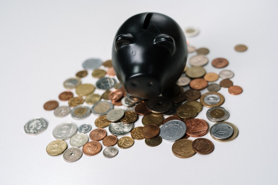 A collection of different currency coins (Euros, Pounds, Dollars) next to a small piggy bank, symbolizing diverse saving goals and exchange rates.