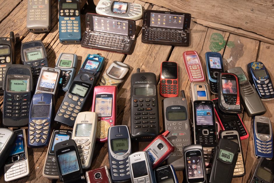An assortment of outdated electronic devices, including a desktop monitor, keyboard, and several mobile phones, neatly stacked for recycling.