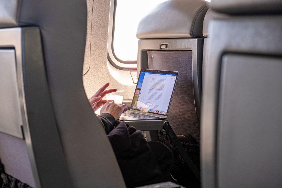 A portable power bank connected via USB-C to a laptop on an airplane tray table, demonstrating efficient in-flight charging.