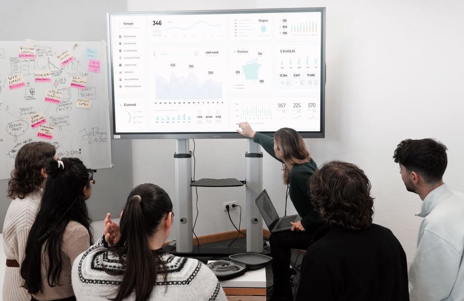A small business team, possibly in a modern office or coworking space, collaborating and discussing a clear, visual CRM dashboard displayed on a large monitor.