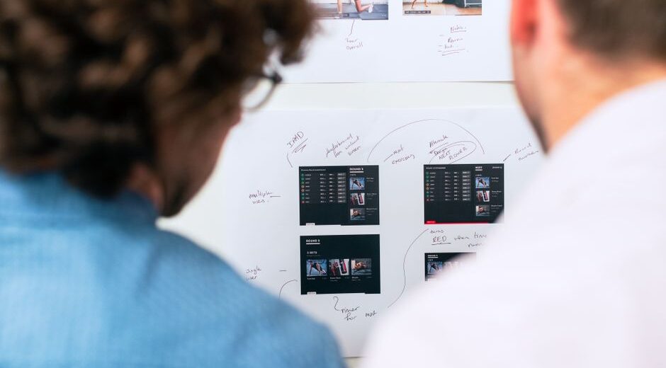 A small, diverse team of professionals collaboratively working on laptops, with a holographic AI interface projecting from a tablet showing data and tasks.
