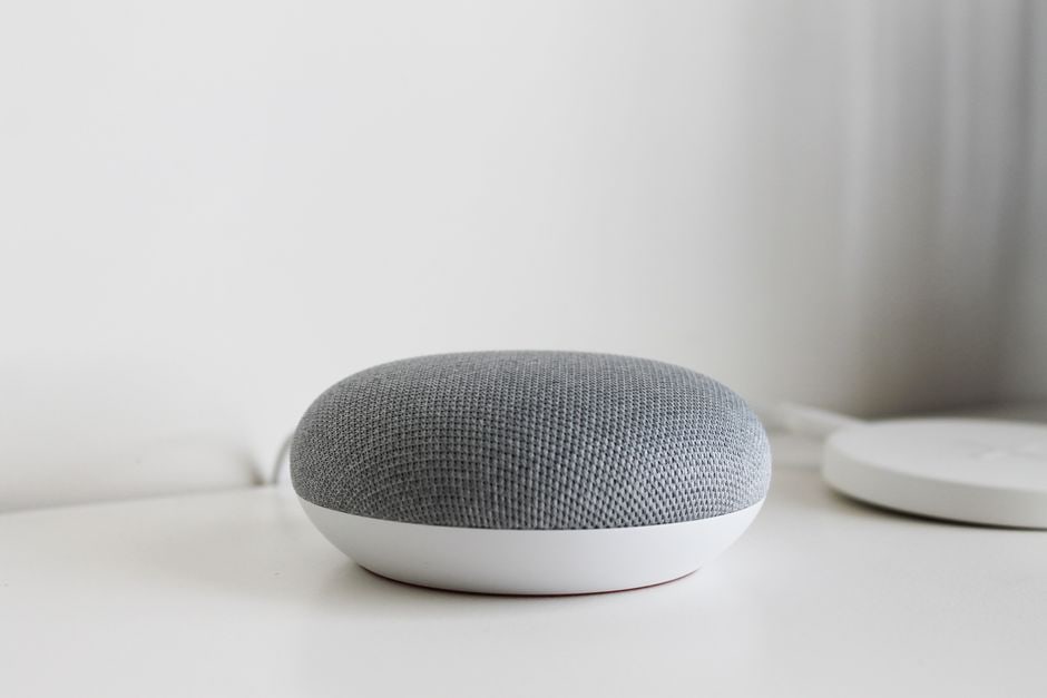 Close-up of smart home devices like a smart plug, voice assistant, and a mesh Wi-Fi router on a desk, representing integrated productivity.