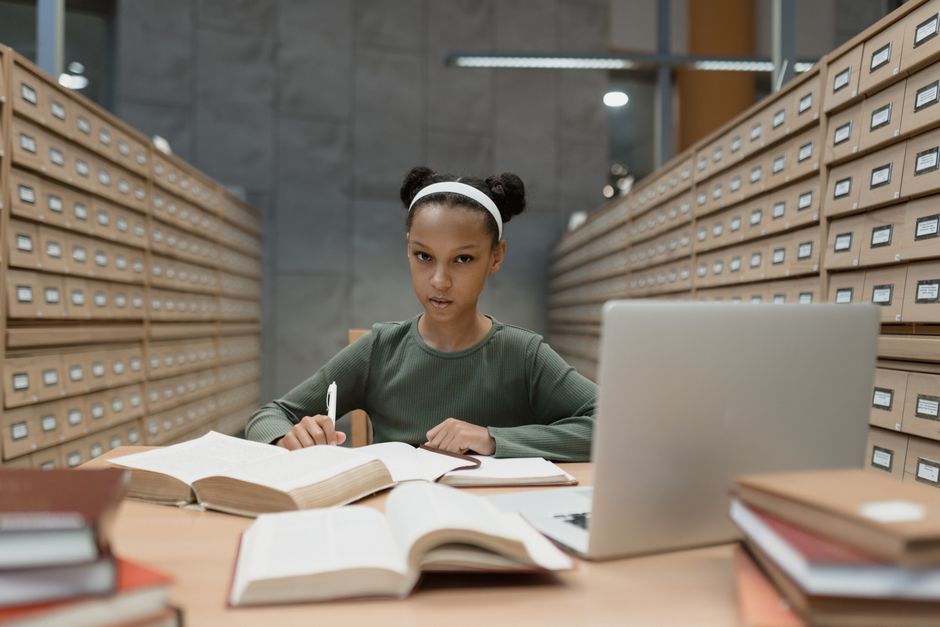 A female student thoughtfully comparing laptop models on a tablet, surrounded by notebooks and pens, embodying the tech buying process.