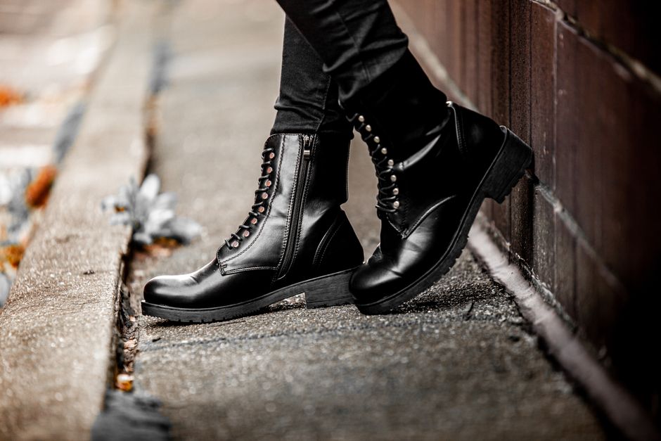 A pair of fashionable dark leather waterproof ankle boots styled for an urban commute, placed on a clean, damp cobblestone street in a European city.