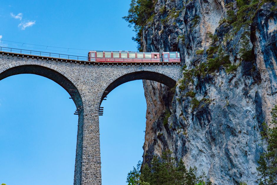 Red Bernina Express train crossing the Brusio spiral viaduct in the Swiss Alps, surrounded by green landscape.
