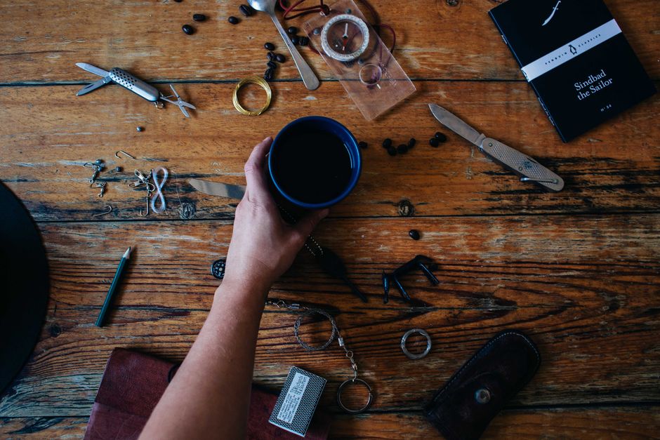 A neatly arranged flat lay of various practical items: an insulated water bottle, a power bank, a small notebook, a gourmet coffee bag, and a hand cream.