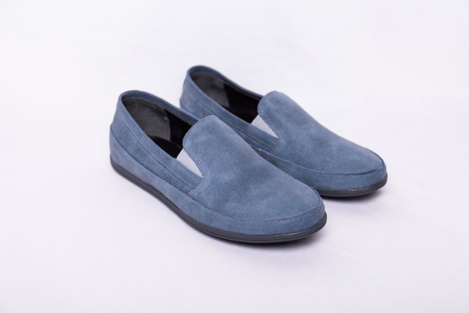 Three distinct pairs of comfortable footwear — classic brown leather loafers, clean white leather trainers, and stylish dark suede Chelsea boots — arranged neatly on a wooden floor.