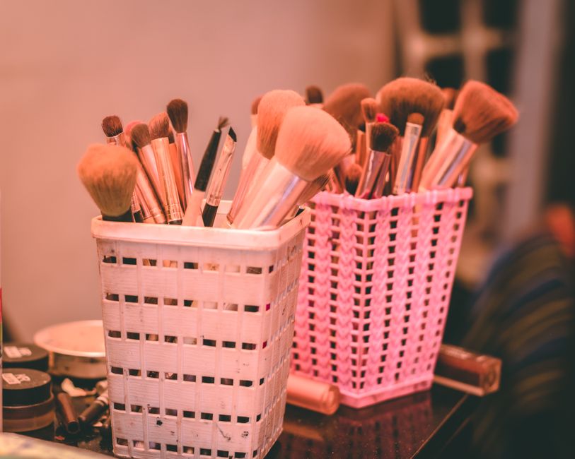 A collection of compact, travel-sized beauty and skincare products including sunscreen, primer, and setting spray, arranged neatly on a hotel vanity.