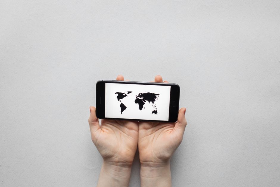 Person holding a smartphone with a world map overlay, illustrating global connectivity and secure browsing while traveling.