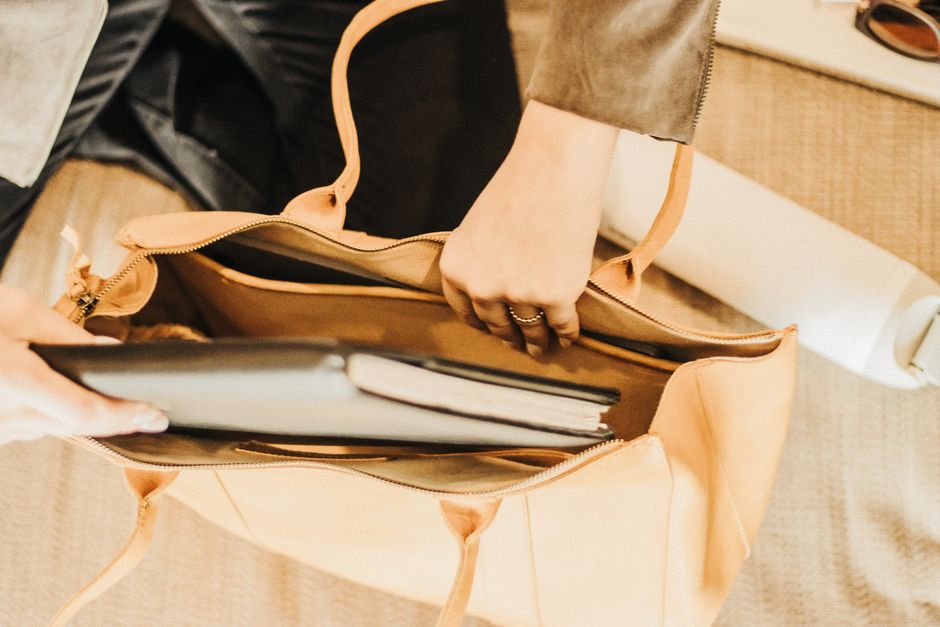 Close-up of a hand cleaning the padded laptop compartment inside a fabric travel bag, removing dust and debris.