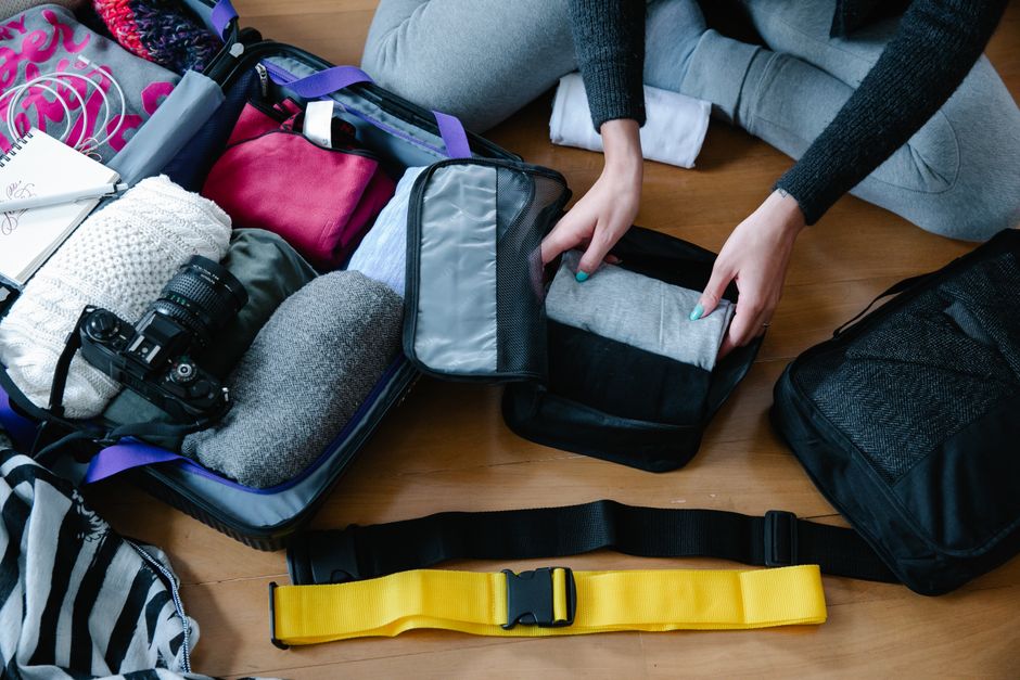A traveler efficiently placing folded clothes into a packing cube inside an open suitcase, illustrating smart travel packing.