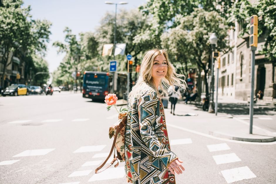 A stylish woman walking with a carry-on suitcase through a European city street, possibly Rome or Florence, enjoying her trip without heavy luggage.