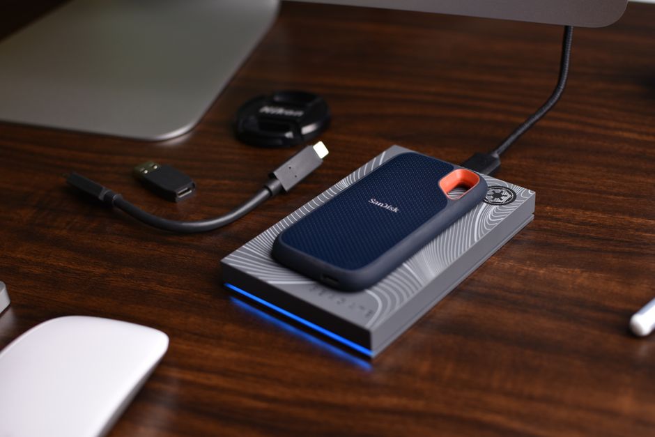 A hand holding a modern smartphone connected via a USB-C cable to a sleek, portable SSD drive, showing external data transfer.