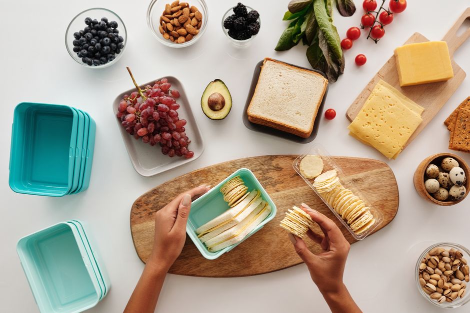 An assortment of easy healthy food ideas for travel, including fruit, nuts, crackers, and veggies, displayed in various reusable food storage containers.