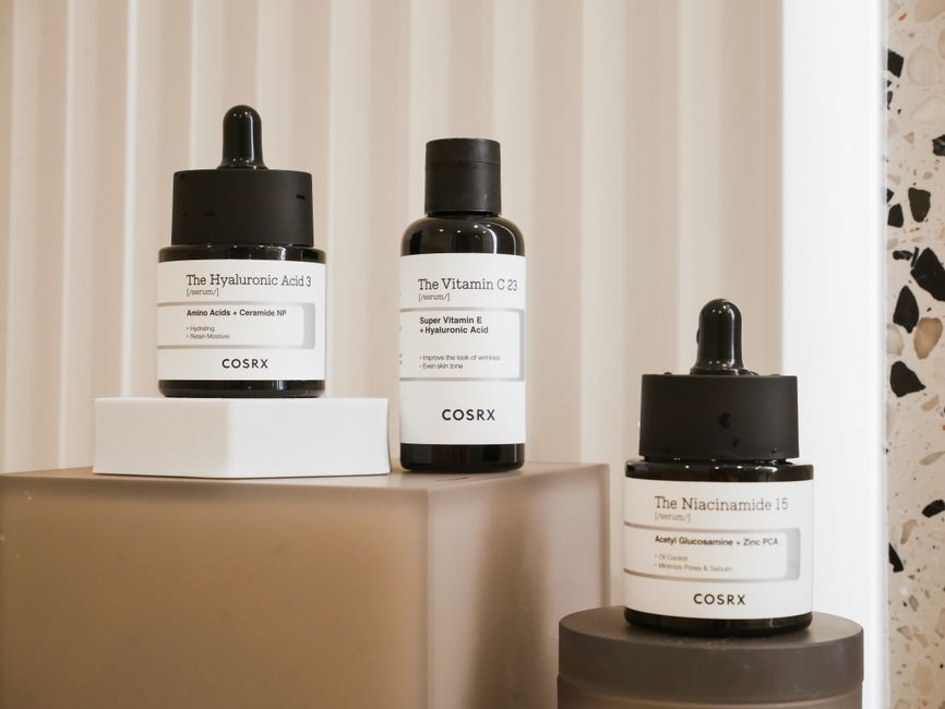 Arrangement of skincare bottles and jars, some labeled with ingredients like hyaluronic acid, glycerin, and ceramides, on a clean, minimalist background.