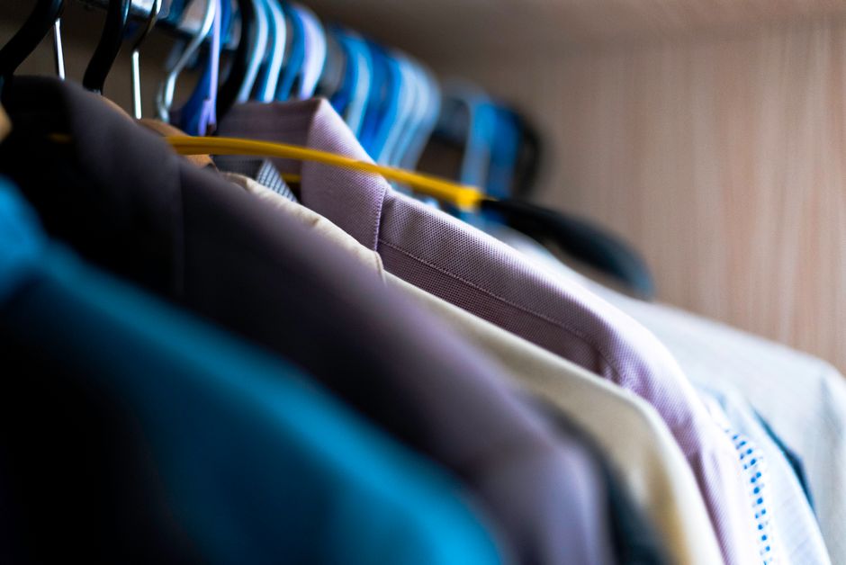 A well-organized men's wardrobe on a rail featuring classic, neutral-colored garments like shirts, sweaters, and trousers, embodying minimalism.