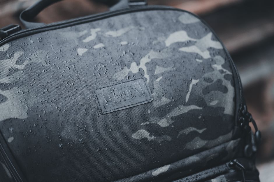 A stylish, dark-colored laptop backpack with water-resistant fabric being worn by someone in a light drizzle, highlighting durability.