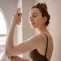 A woman in a comfortable airplane seat delicately mists her face with a hydrating spray, her eyes closed in relaxation, emphasizing in-flight skincare.