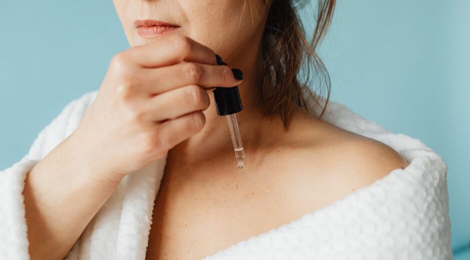 A woman gently patting a hydrating serum onto her face, which has water droplets visible, in a bright bathroom.