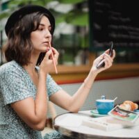 Woman thoughtfully applying lightweight makeup with a brush on a bright, sunny day, suggesting a fresh, natural summer look.