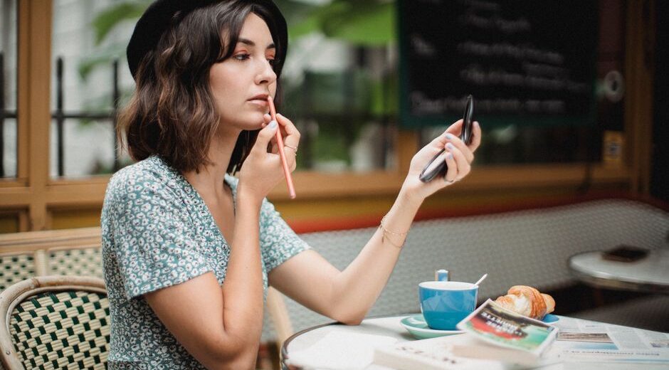 Woman thoughtfully applying lightweight makeup with a brush on a bright, sunny day, suggesting a fresh, natural summer look.