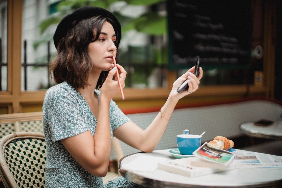 Woman thoughtfully applying lightweight makeup with a brush on a bright, sunny day, suggesting a fresh, natural summer look.