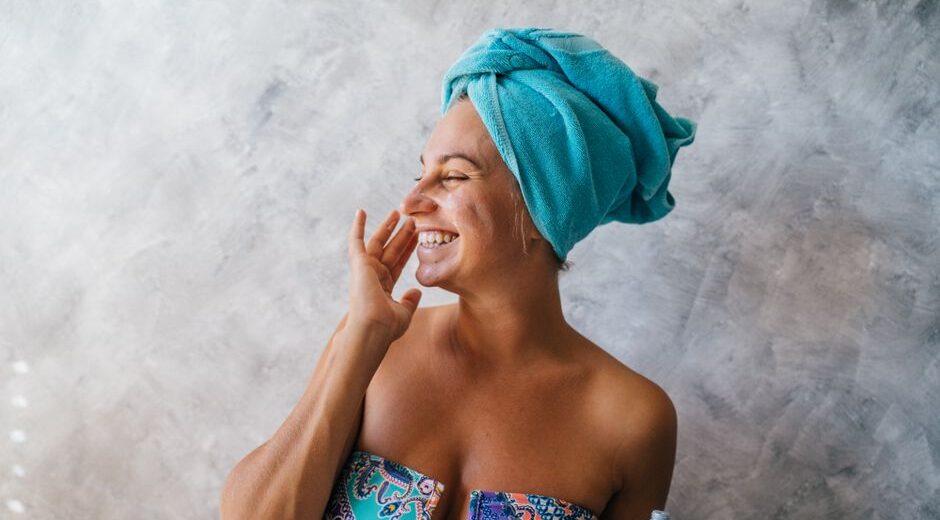 A smiling woman gently applying a moisturizer to her cheek after cleansing, highlighting a simple beauty routine.