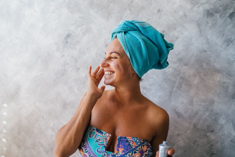 A smiling woman gently applying a moisturizer to her cheek after cleansing, highlighting a simple beauty routine.