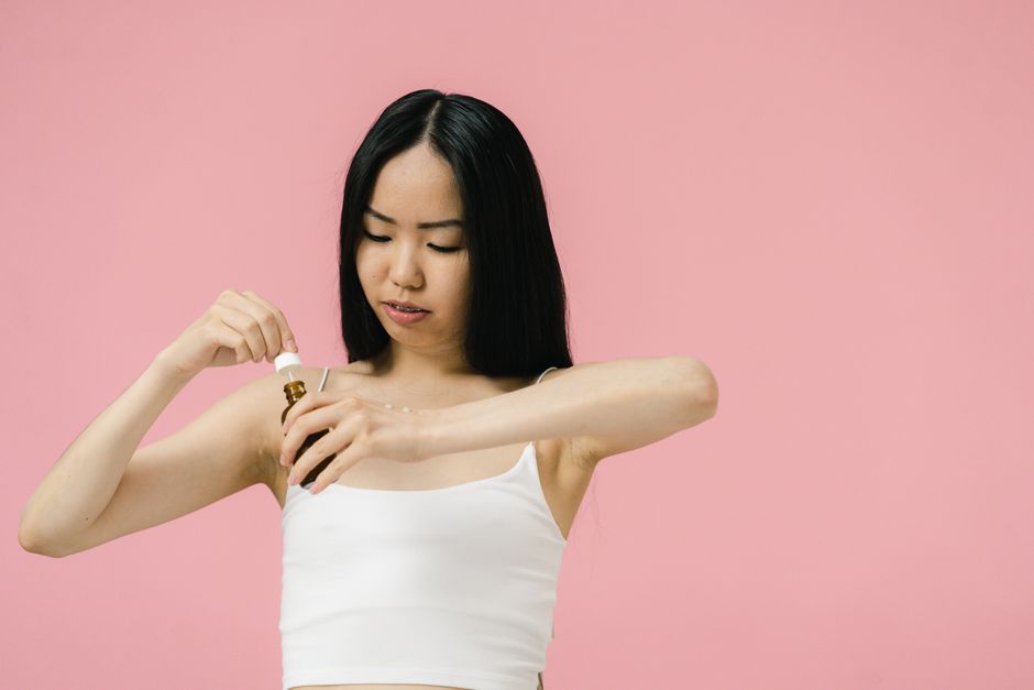 A person carefully applying a few drops of vitamin C serum to their face, focusing on a targeted treatment for skin brightening.