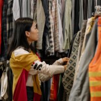 A woman thoughtfully examining a blouse on a hanger in a brightly lit, minimalist sustainable fashion store.