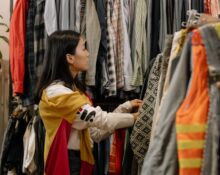 A woman thoughtfully examining a blouse on a hanger in a brightly lit, minimalist sustainable fashion store.