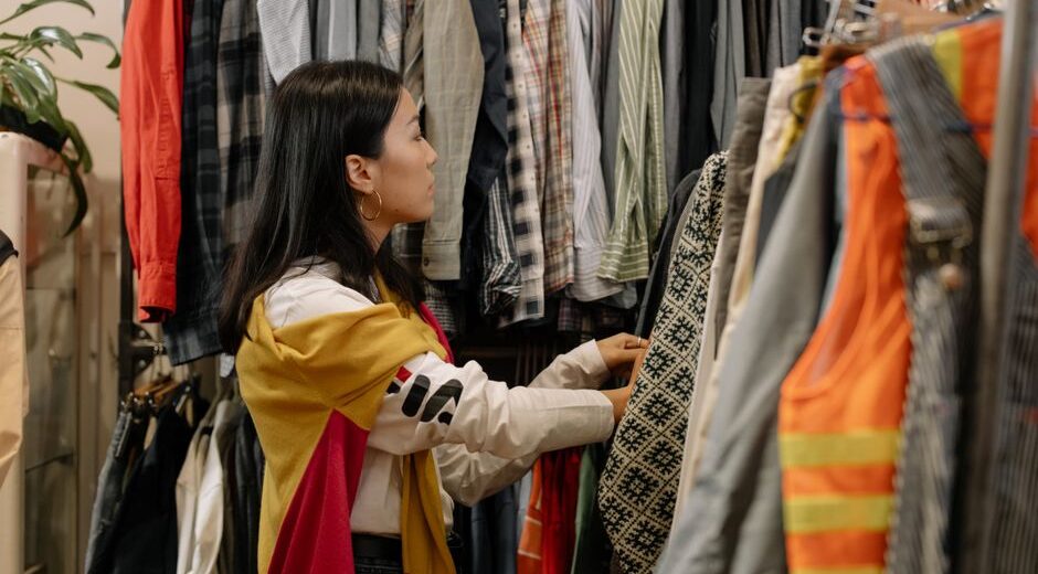 A woman thoughtfully examining a blouse on a hanger in a brightly lit, minimalist sustainable fashion store.