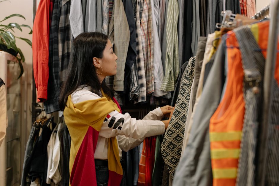A woman thoughtfully examining a blouse on a hanger in a brightly lit, minimalist sustainable fashion store.