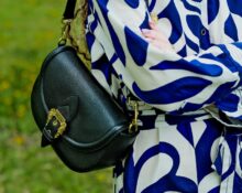 A woman carefully wiping down her brown leather crossbody bag with a soft cloth, demonstrating gentle cleaning.