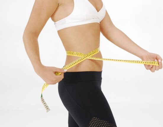 A woman in light clothing carefully measuring her waist with a soft tape measure, focusing on accurate body measurements for online shopping.