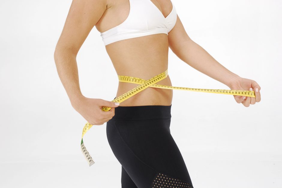 A woman in light clothing carefully measuring her waist with a soft tape measure, focusing on accurate body measurements for online shopping.