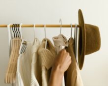 Woman thoughtfully arranging various neutral clothing items in a minimalist capsule wardrobe, demonstrating versatility.