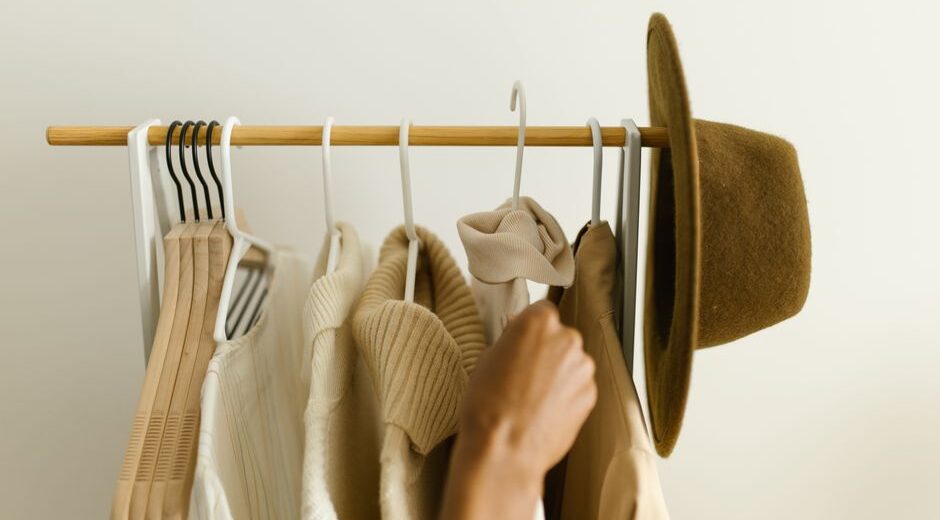 Woman thoughtfully arranging various neutral clothing items in a minimalist capsule wardrobe, demonstrating versatility.