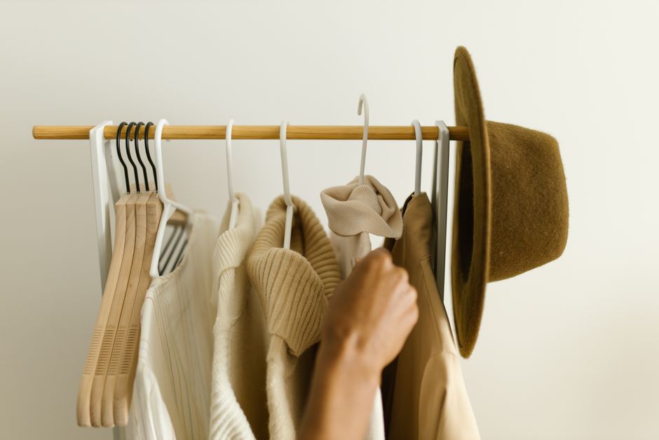 Woman thoughtfully arranging various neutral clothing items in a minimalist capsule wardrobe, demonstrating versatility.